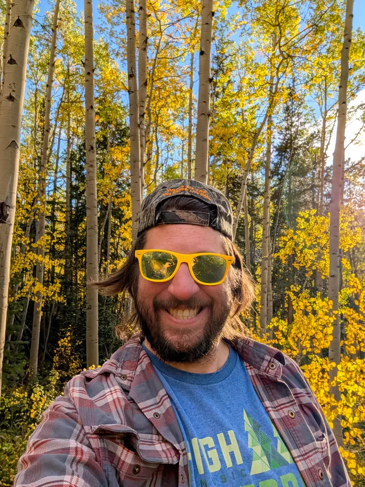 Lee Driggers smiling in yellow sunglasses among golden aspen trees.